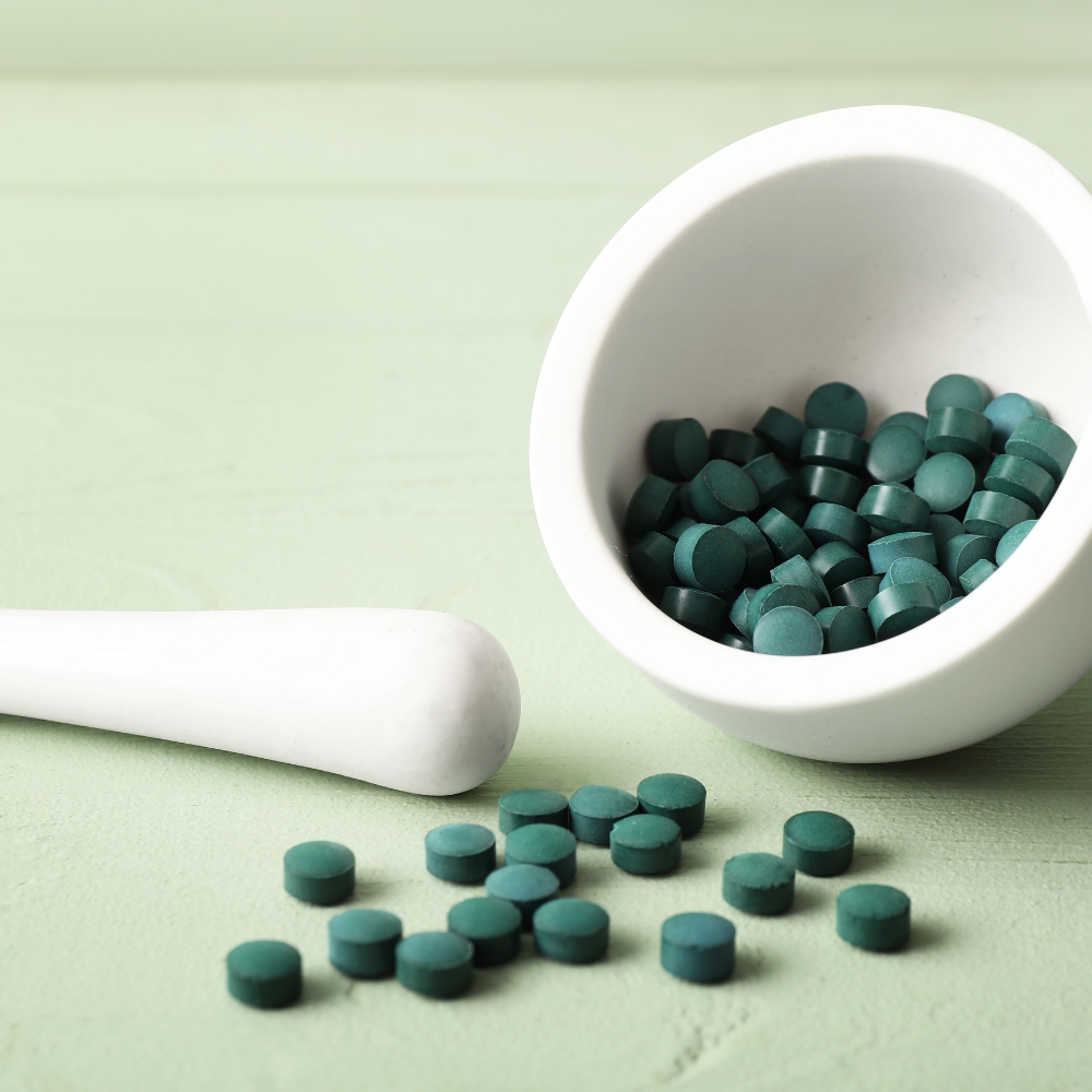Green pills in a white mortar and pestle on a light green background